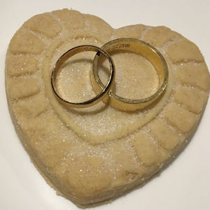 Two gold wedding rings on a heart-shaped
                    shortbread biscuit