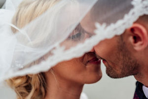 White bride and groom kissing under bridal
                    veil