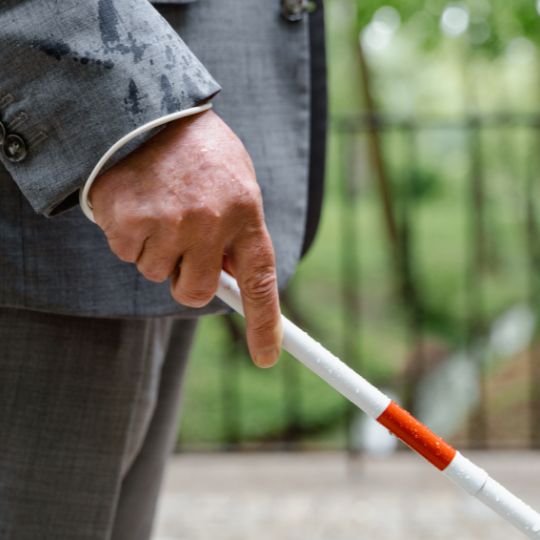 Man wearing a gray suit and using a white
                        cane