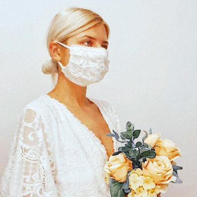 Bride wearing white lace mask and carrying a
                      bouquet of apricot roses