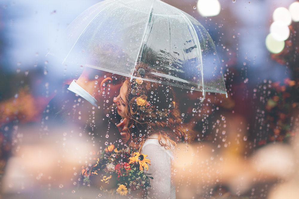 Bride and Groom under an umbrella in pouring
                  rain