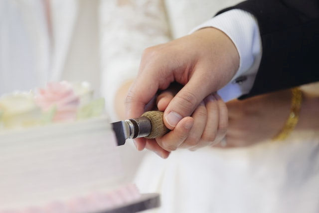 Close up of joined hands
                      cutting a cake